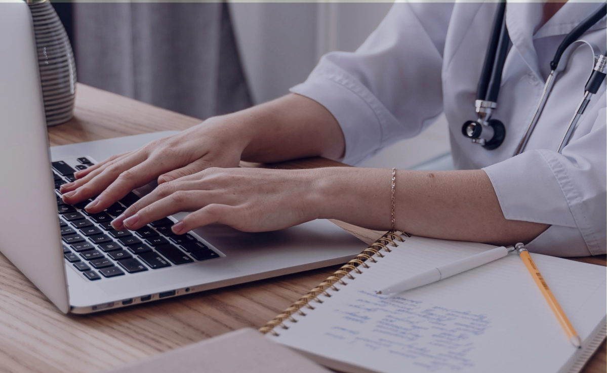 Healthcare professional typing clinical reports on laptop - Acuity Health Solutions